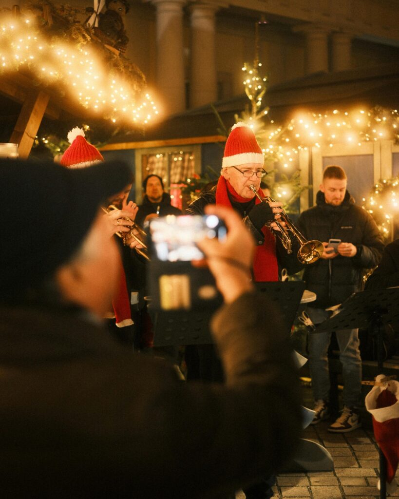 Joyful brass band performing at a Christmas market with festive decorations and lights.